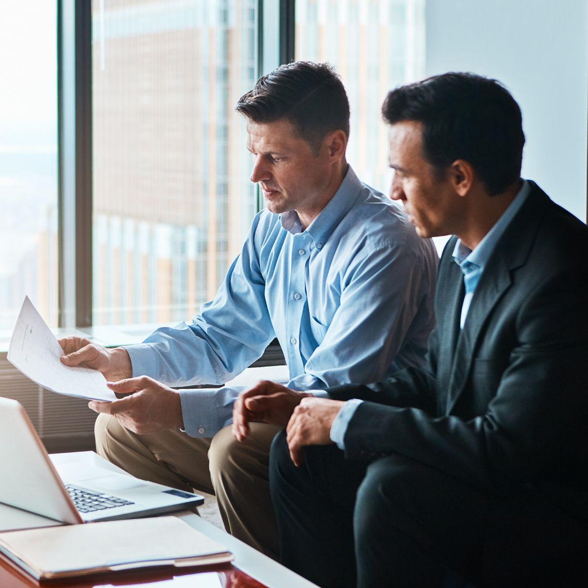 Dos hombres de negocios revisando documentos en una oficina, representando asesoría para la reactivación de derechos en el IMSS.